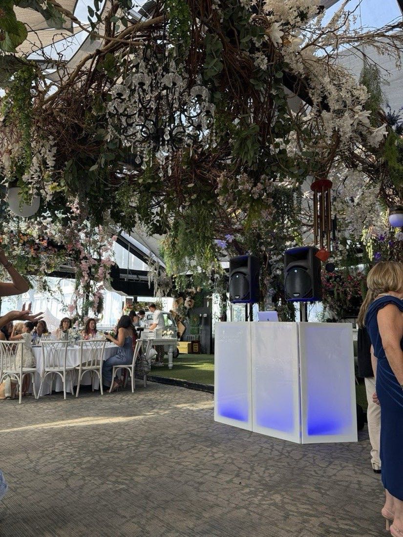 White DJ facade with blue LED booth lighting and speakers under the floral canopy at Angelina's Ristorante, Staten Island