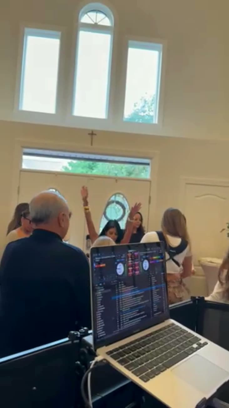 View from behind the DJ booth at a New Jersey housewarming party, guests dancing with hands up